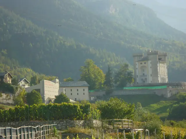 Cave des Onze Communes' winery building (its name in red on the facade) below Aymavilles castle, vines in front, hazy autumn light