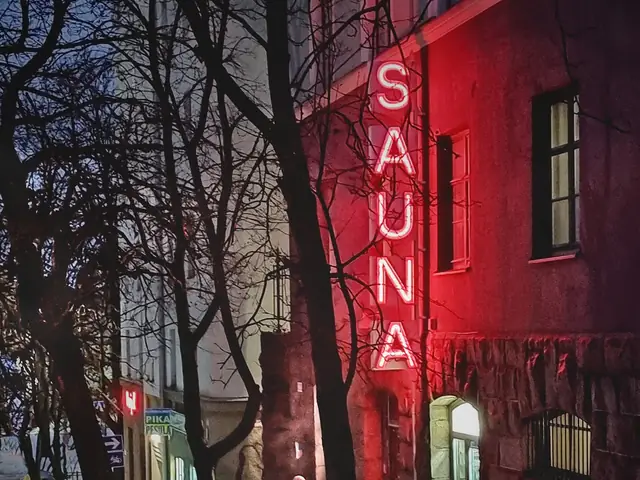 Kotiharju sauna at night: the red SAUNA neon on the granite-based facade, snow on the street