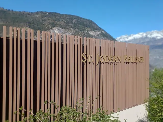 The St. Jodern Kellerei's slatted facade with its name in gold letters, snowy Valais peaks behind