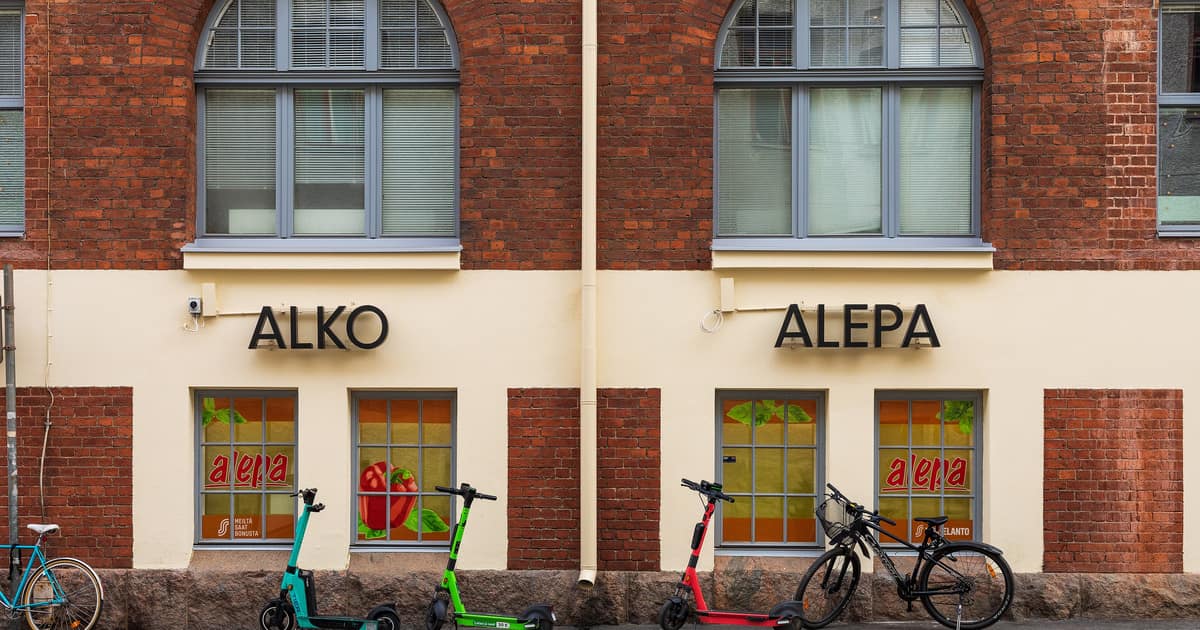 An ALKO sign beside an ALEPA sign on a red-brick building in Helsinki, scooters parked outside