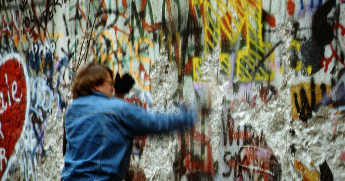 A man in a denim jacket chipping pieces off the graffiti-covered Berlin Wall in 1989