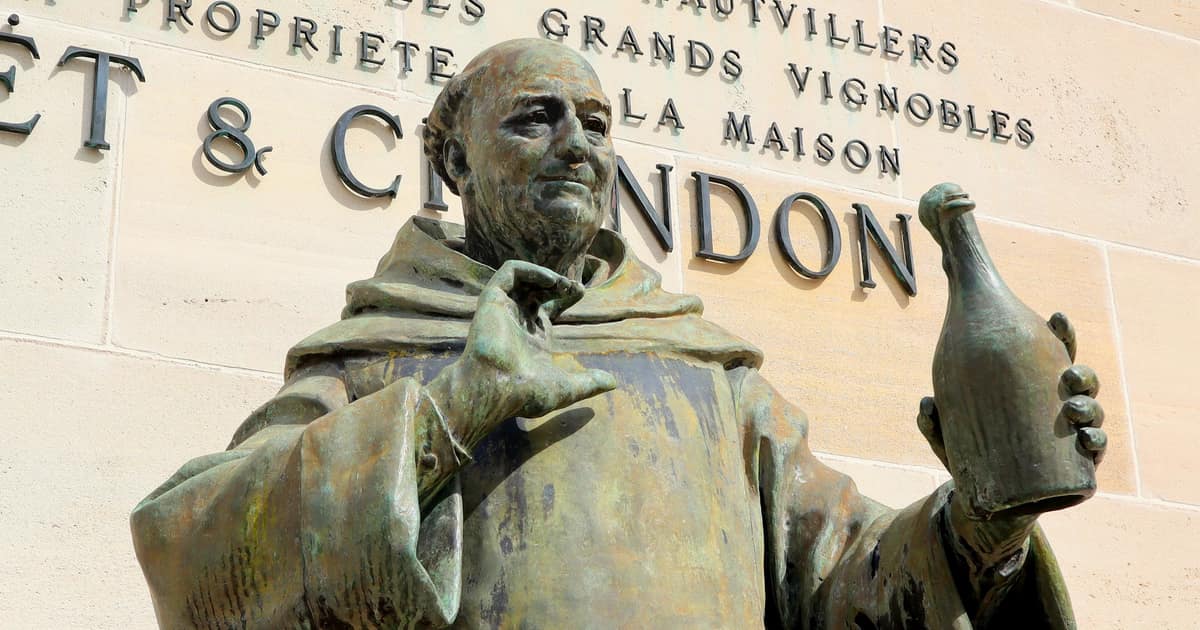 Bronze statue of the monk Dom Pérignon holding up a bottle, in front of the Moët & Chandon wall