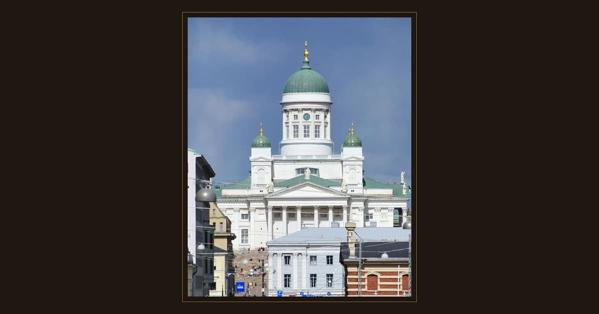 The white Helsinki Cathedral with its green dome at the end of a busy street