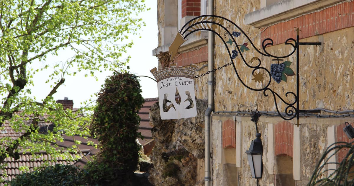 An ornate wrought-iron sign with grapes hanging from an old stone house in Hautvillers