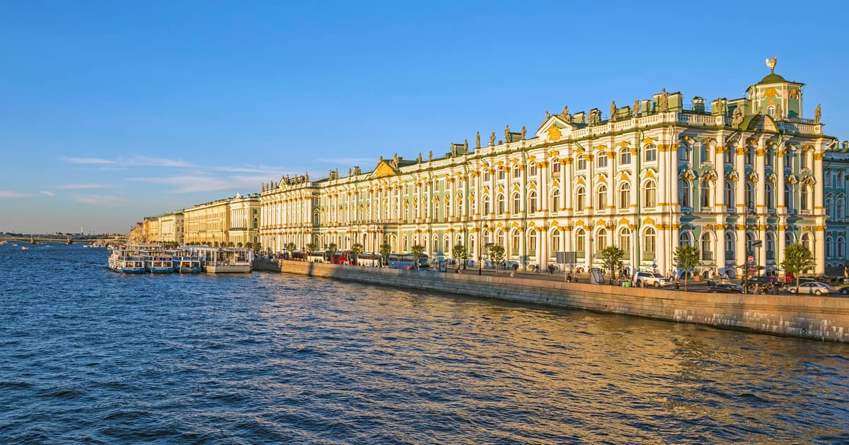 The long green-and-white facade of the Winter Palace along the Neva embankment in evening sun