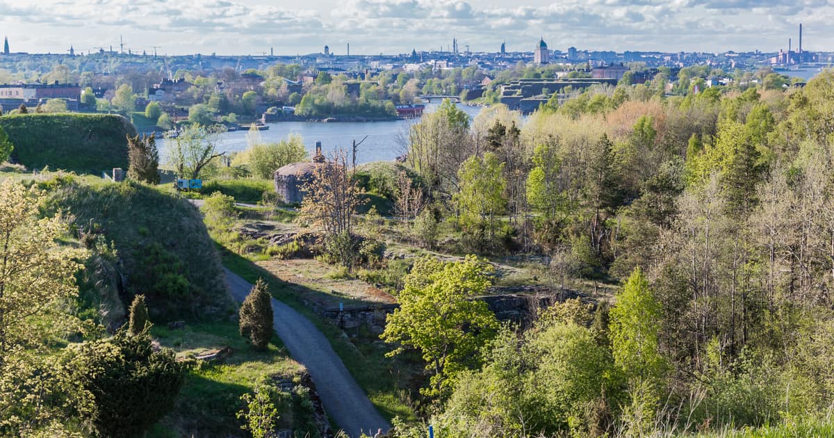 Green fortress slopes and a path on Vallisaari island, the Helsinki skyline across the sea