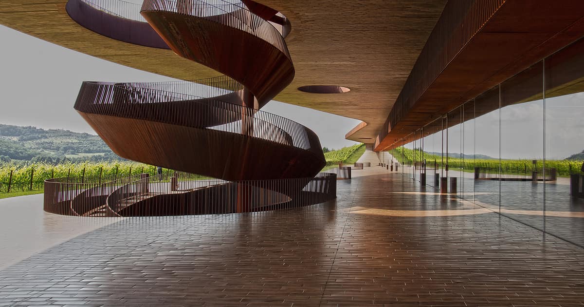 A sculpted spiral staircase inside the Antinori winery, vineyards beyond the glass wall